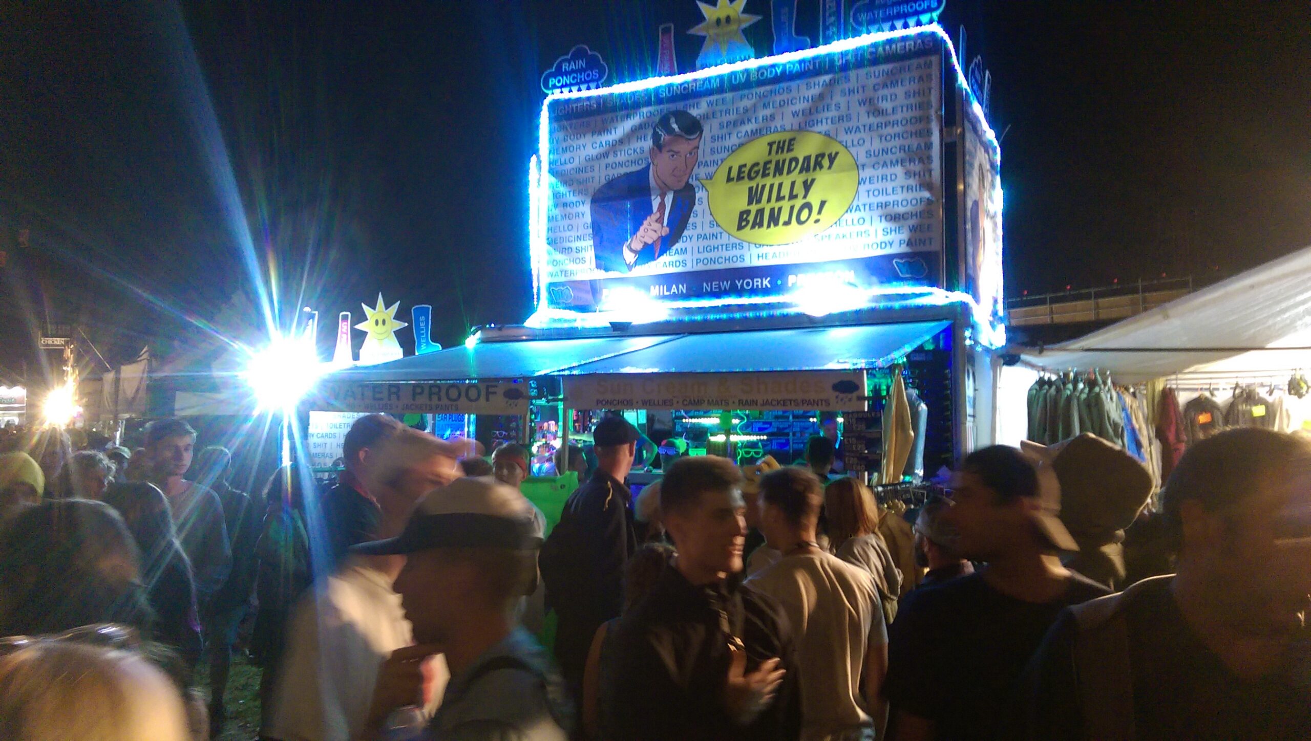 The Willy Banjo stall at Glastonbury — daytime, full display with neon lanyards and sunglasses