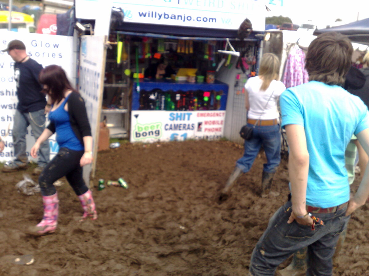 Festival-goers in wellies wading through mud outside the Willy Banjo stall