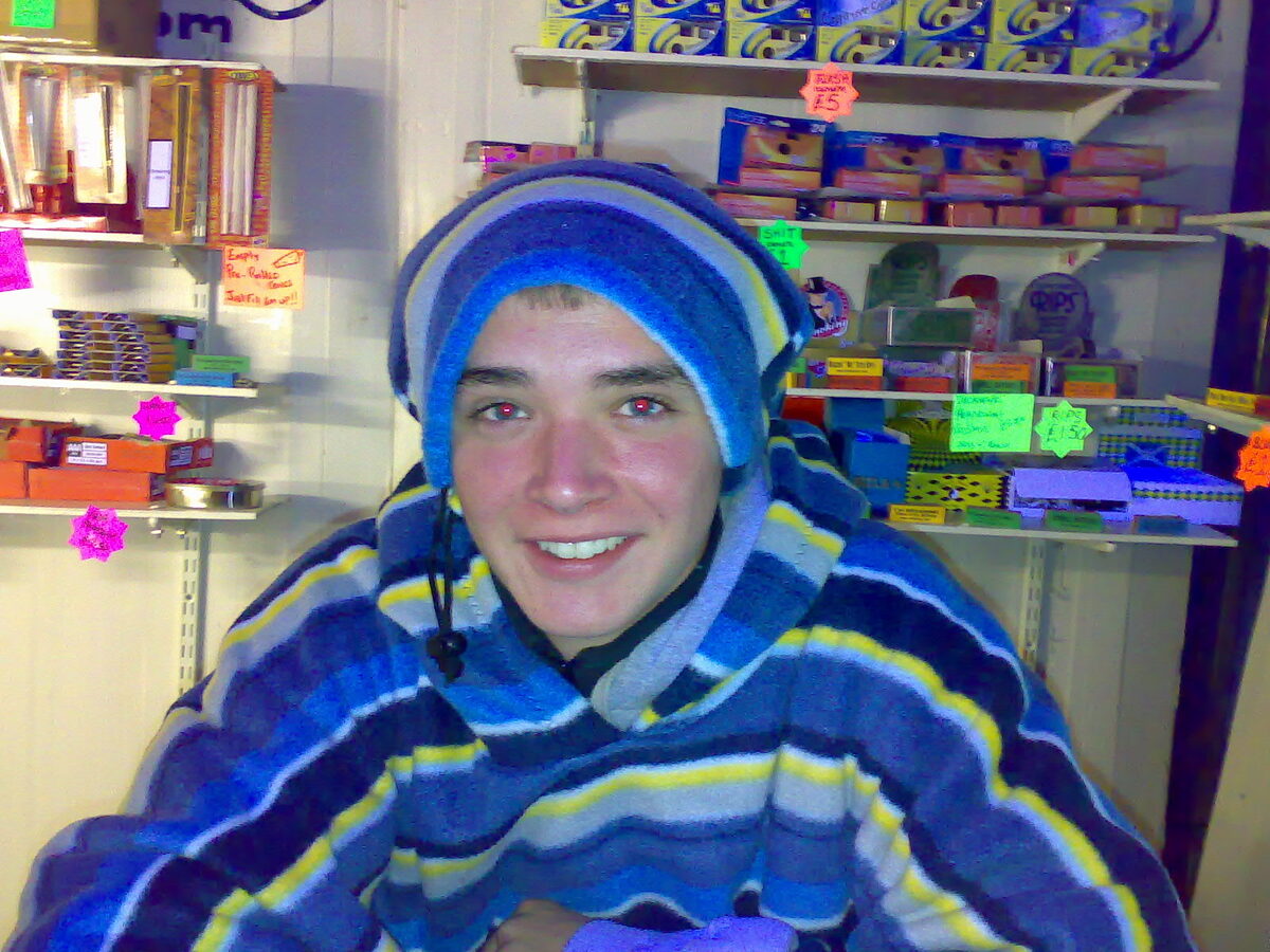 A festival-goer wrapped in a blanket, smiling in the stall