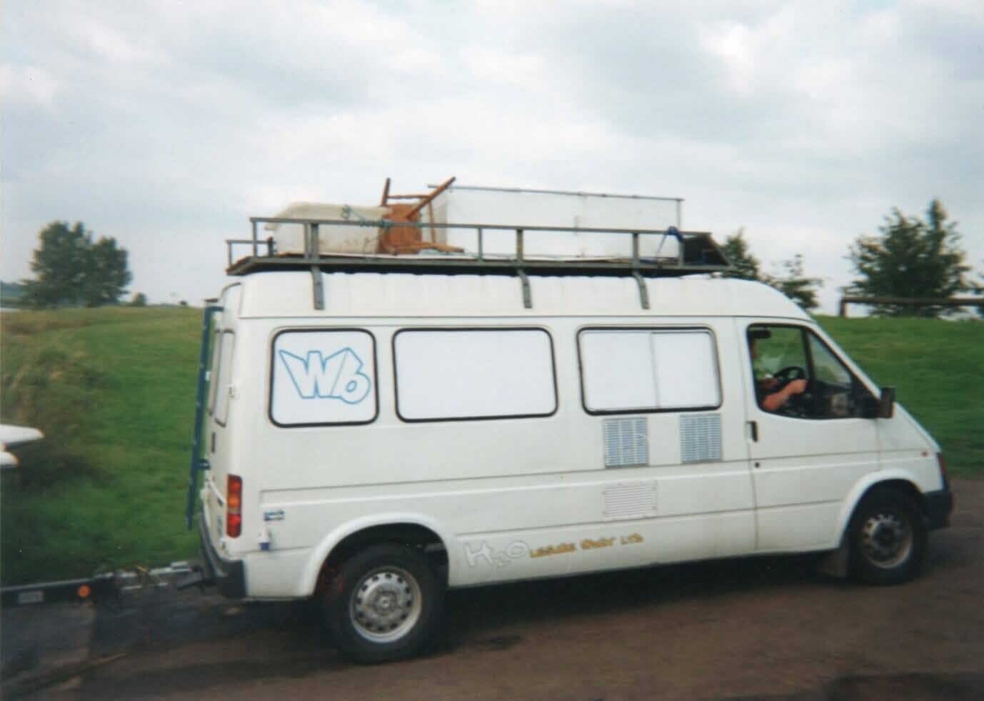 Overloaded Willy Banjo Ford Transit van with a chair strapped to the roof rack at a festival