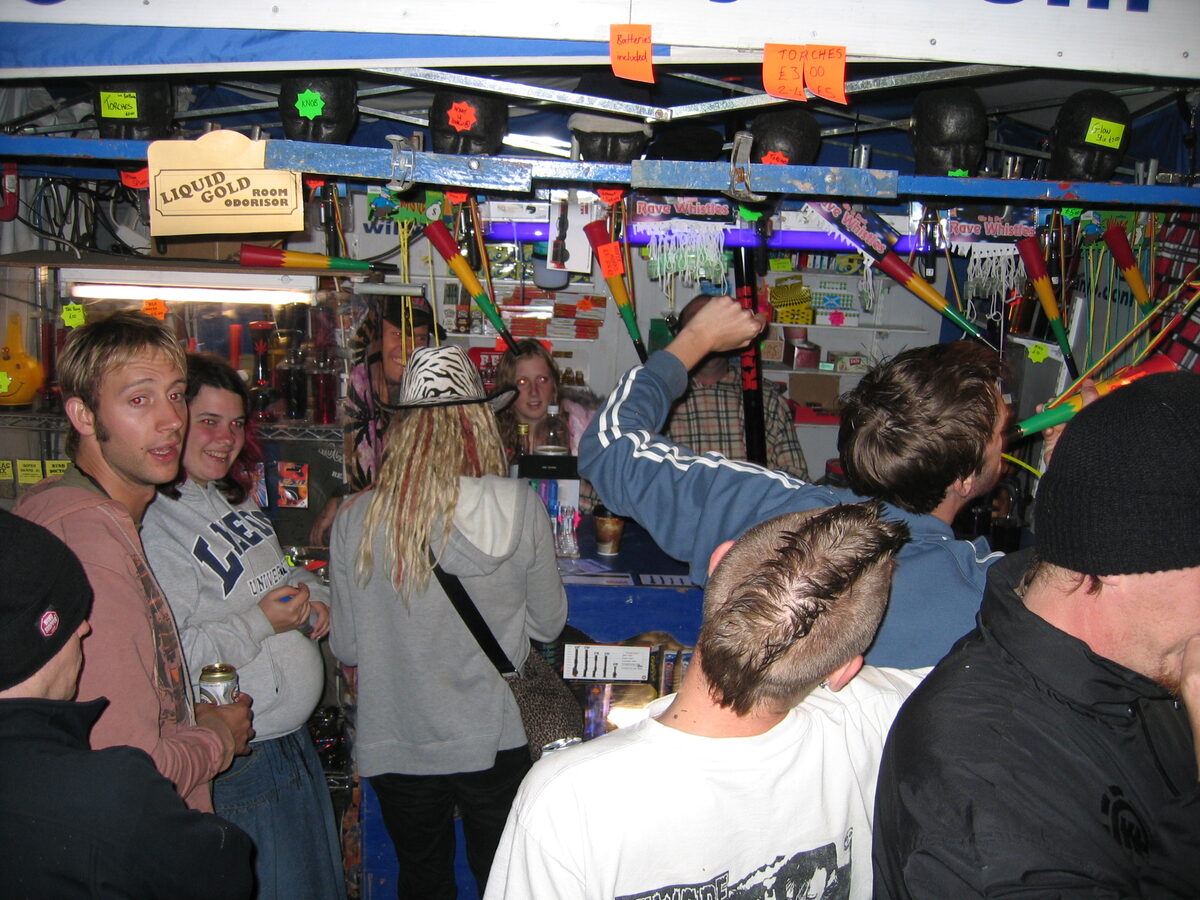 Crowd inside the Willy Banjo stall at night buying rave whistles under UV light